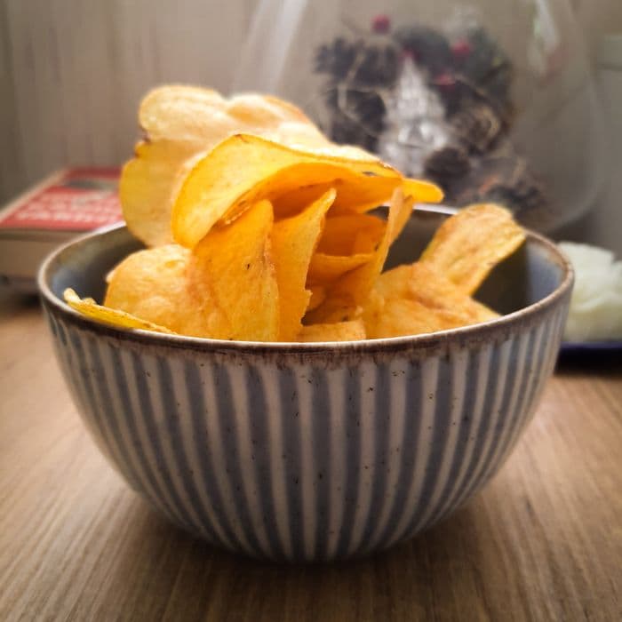 Golden potato chips in a striped ceramic bowl