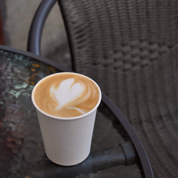 A latte with poured art in a takeaway cup on a cafe table